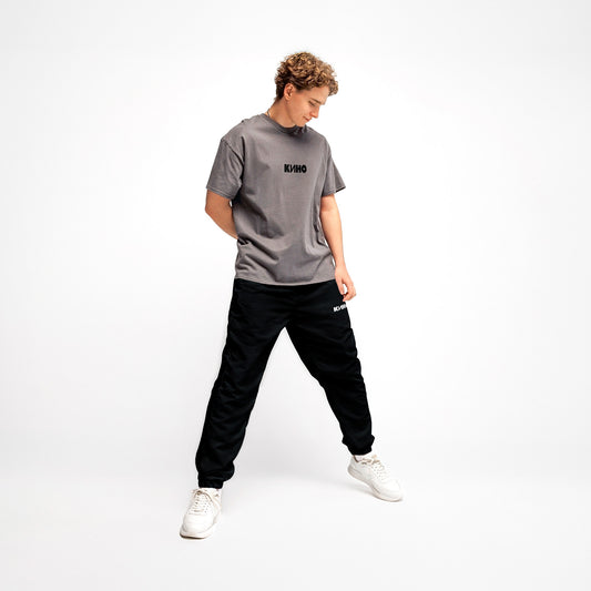 Young handsome white-skinned boy model wearing black official KINO band sport pants like Viktor Tsoi had. With KINO logo on the left pant. Premium cuffed joggers. Front side. From www.kinoband.com