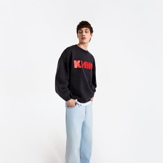 Young male boy model in photostudio wearing black sweatshirt with large red KINO Band logo and Viktor Tsoi necktag. From kinoband.com
