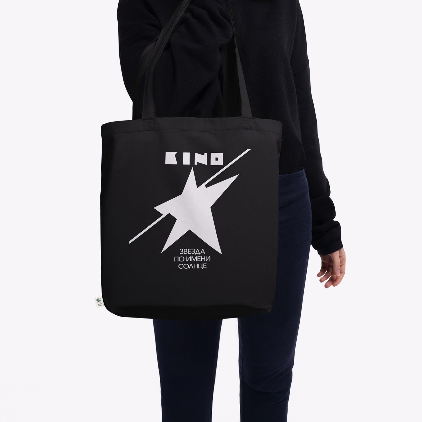 Model wearing official KINO band black organic cotton tote bag featuring a double-sided print: the Zvezda po imeni Solntse white star album art on one the front side and the KINO (КИНО) classic logo on the the reverse. www.kinoband.com