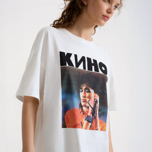 Cute young model girl wearing white t-shirt with large photo of Viktor Tsoi performing live and bold KINO band logo above. From kinoband.com