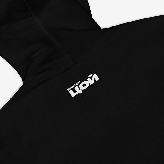 Official black unisex KINO band hoodie featuring an original colorful painting by Viktor Tsoi with a small КИНО logo underneath, with small "Виктор Цой” logo in Cyrillic on the back. Back side closeup photo. www.kinoband.com