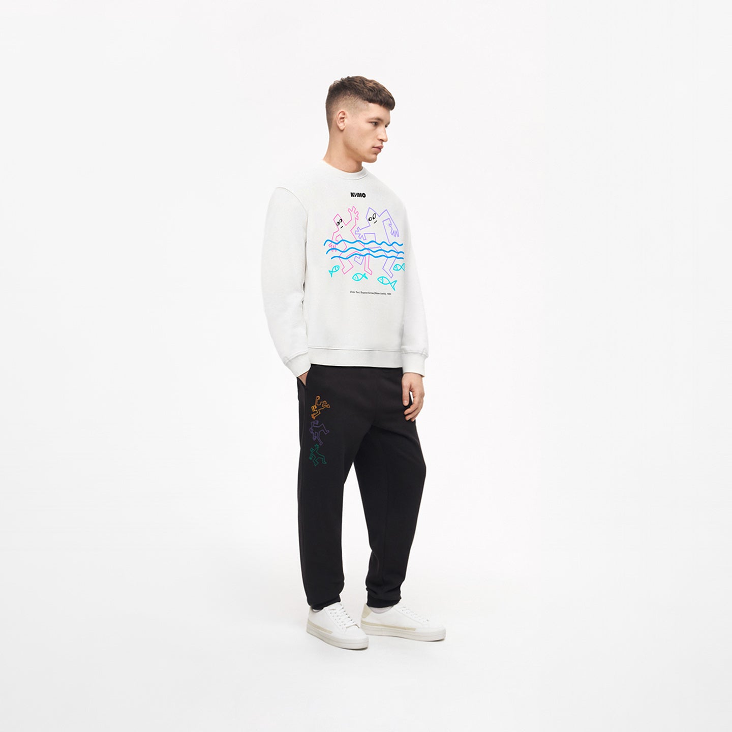 Handsome young white-skinned man wearing official white unisex KINO band sweatshirt featuring original painting by Viktor Tsoi and small КИНО logo. www.kinoband.com