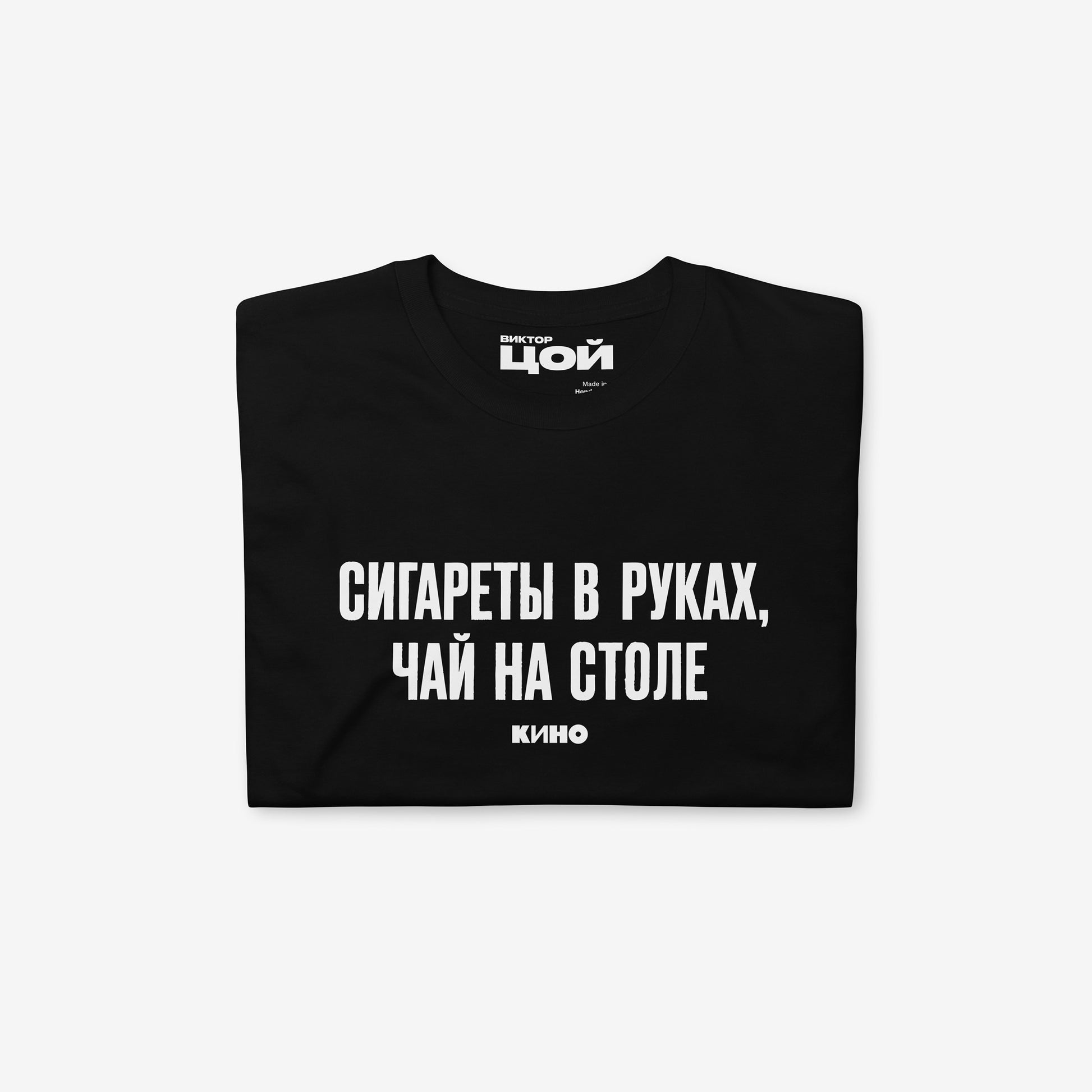 Official KINO Band black unisex T-shirt featuring lyrics in bold russian from a 'Peremen' (Перемен – Change) song by Viktor Tsoi 'Cigarettes in hands, tea on the table' (Сигареты в руках, чай на столе) and КИНО logo underneath. Folded. www.kinoband.com