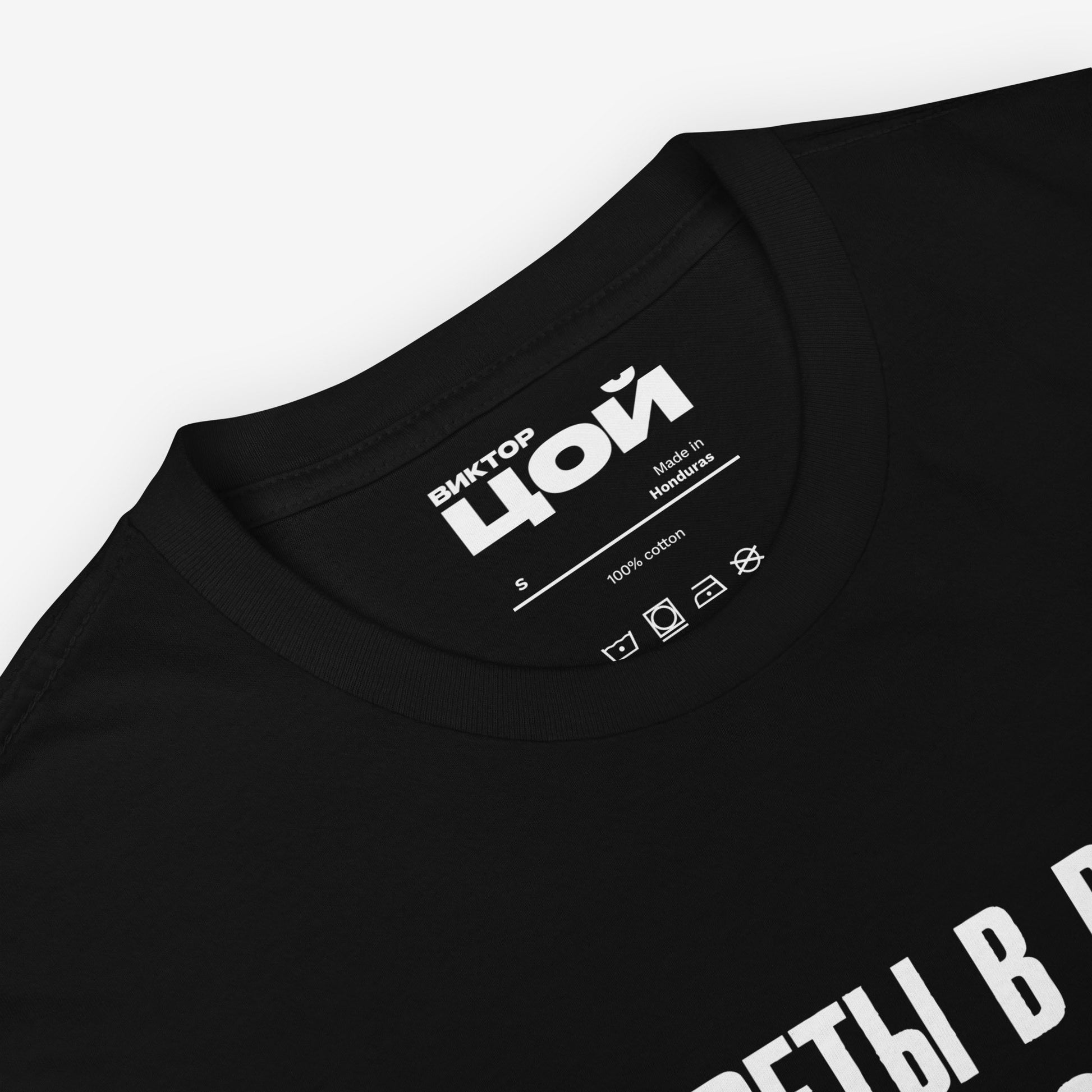 Official KINO Band black unisex T-shirt featuring lyrics in bold russian from a 'Peremen' (Перемен – Change) song by Viktor Tsoi 'Cigarettes in hands, tea on the table' (Сигареты в руках, чай на столе) and КИНО logo underneath. Closeup necktag print details with Виктор Цой logo. www.kinoband.com