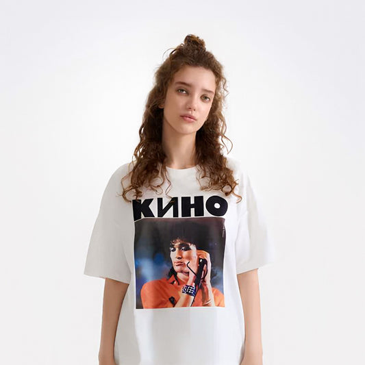 Cute young model girl wearing white t-shirt with large photo of Viktor Tsoi performing live and bold KINO band logo above. From kinoband.com