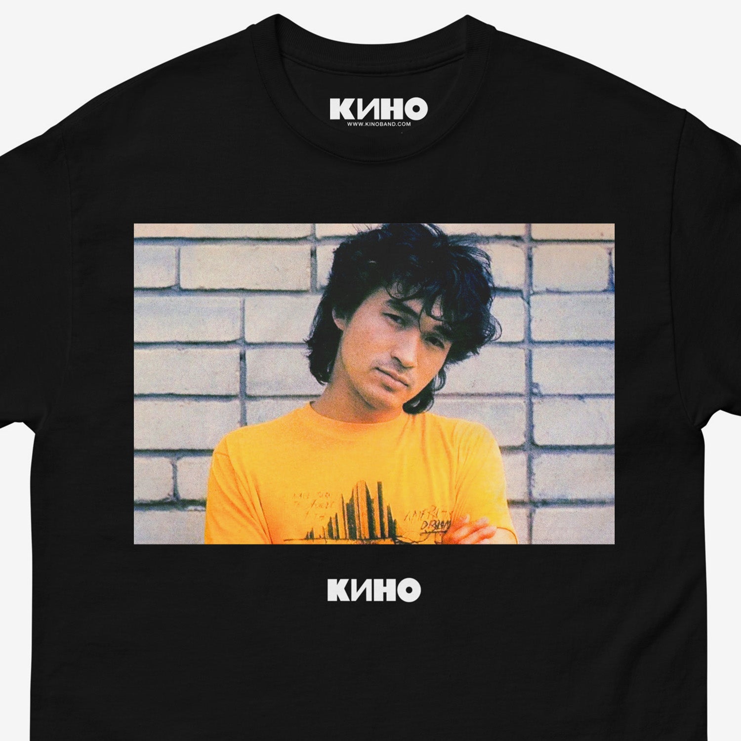 Official KINO band shirt with large print of Viktor Tsoi wearing yellow tee against a white brick wall, with Группа КИНО logo under the photo. Closup details. www.kinoband.com